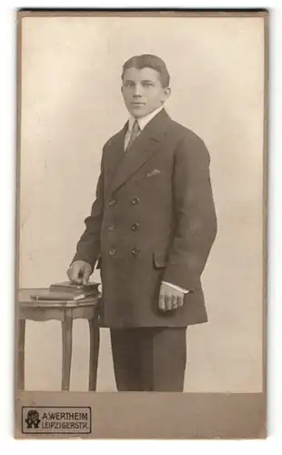Fotografie A. Wertheim, Berlin, Portrait junger Herr im Anzug mit Büchern an Tisch gelehnt