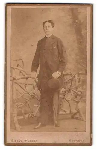 Fotografie Gustav Wetzel, Dresden, Portrait junger Herr im Anzug mit Hut an Zaun gelehnt