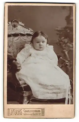 Fotografie J. Fuchs, Berlin-Charlottenburg, Portrait niedliches Kleinkind im hübschen Kleid auf Stuhl sitzend