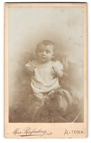 Fotografie Max Reifenberg, Altona, Portrait niedliches Baby im weissen Hemd auf Fell sitzend