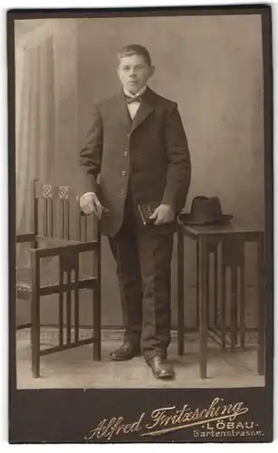 Fotografie Alfred Fritzsching, Löbau i. S., Portrait charmanter junger Mann mit Buch und Hut im Anzug