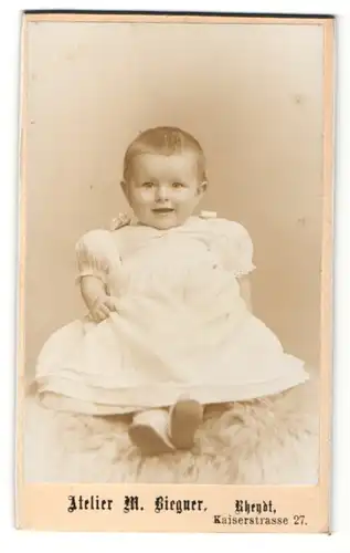 Fotografie M. Biegner, Rheydt, Portrait niedliches Kleinkind im hübschen Kleid auf Fell sitzend