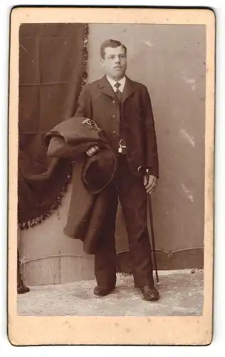 Fotografie Franz Sternath, München, Portrait Herr im Anzug mit Hut, Stock u. Mantel unterm Arm