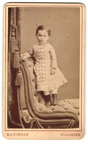 Fotografie M. J. Simson, Dillingen, Portrait kleines Mädchen im hübschen Kleid auf Sessel stehend