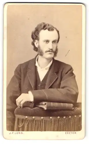 Fotografie J. F. Long, Exeter, Portrait Herr mit Backenbart im Anzug auf Lehne gestützt