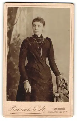 Fotografie Richard Noodt, Hamburg, Portrait Dame im eleganten Kleid mit Halskette an Zaun gelehnt