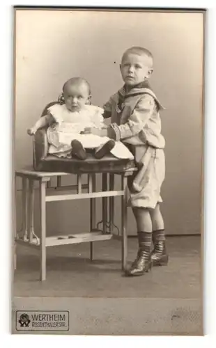 Fotografie Atelier Wertheim, Berlin, Junge im Pfadfinderkleidung stehend und Baby im Kinderstuhl sitzend