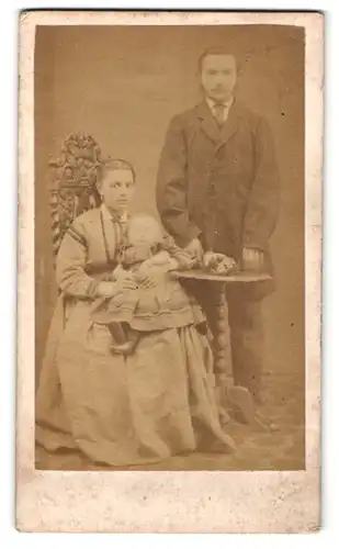 Fotografie F. Cole, London, Mann mit Kotletten im Anzug stehend und Frau im Kleid sitzend mit Baby auf den Armen