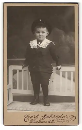 Fotografie Carl Schröder, Dahme i/M., Kind im Anzug mit Mütze auf Bank stehend