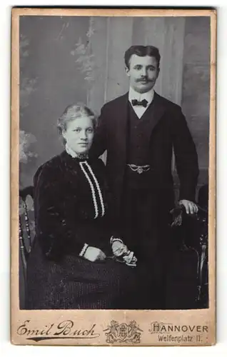 Fotografie Emil Buch, Hannover, Portrait bürgerliches Paar in eleganter Kleidung mit Blume