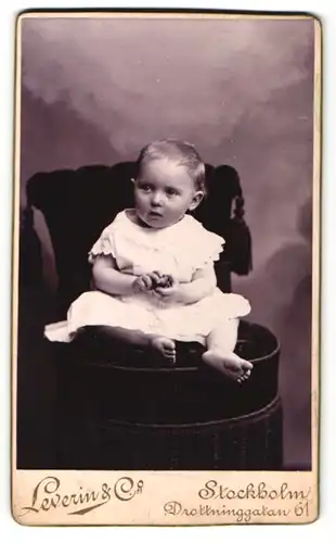 Fotografie Leverin & Co., Stockholm, Kleinkind im Kleidchen auf Sessel sitzend