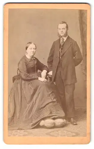 Fotografie Wilhelm Grundner, Berlin, Mann im Anzug mit Backenbart und Frau im Kleid sitzend