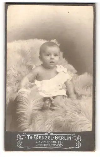 Fotografie Th. Wenzel, Berlin, Portrait niedliches Baby im weissen Hemd auf Fell sitzend