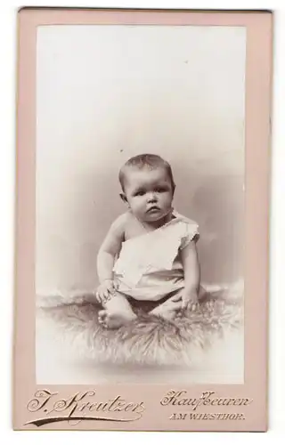 Fotografie J. Kreutzer, Kaufbeuren, Baby im Kleidchen auf Pelz sitzend