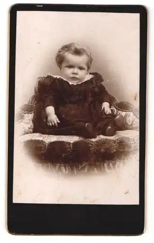 Fotografie unbekannter Fotograf und Ort, Kleinkind in dunklem Kleidchen auf Sessel sitzend
