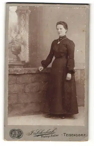 Fotografie J. Schubeck, Teisendorf, Frau im Kleid mit Halskette und Amulett mit Arm auf Wand gestützt