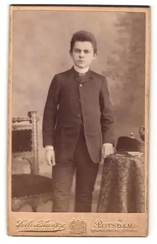 Fotografie Selle & Kuntze, Potsdam, junger Mann im Anzug mit linker Hand auf Tisch gestützt