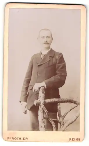 Fotografie Fs. Rothier, Reims, Mann im Anzug mit Schnurrbart stehend an Holzgeländer