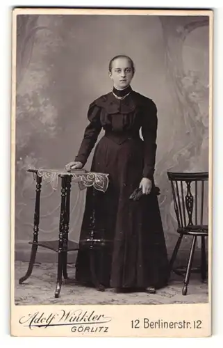 Fotografie Adolf Winkler, Görlitz, Frau im Kleid stehend mit einer Hand auf einem Tisch