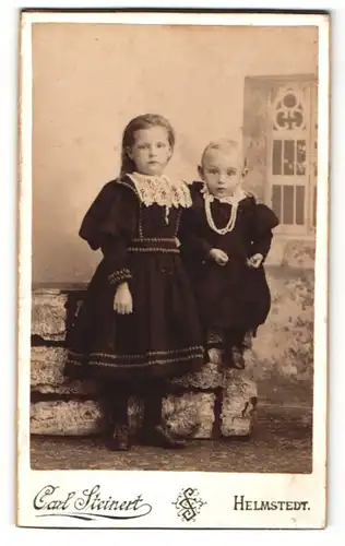Fotografie Carl Steinert, Helmstedt, Mädchen im Kleid stehend und Mädchen im Kleidchen auf Mauern sitzend