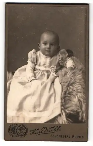 Fotografie Karl Wahl, Berlin, Baby im Kleidchen auf Pelzdecke sitzend