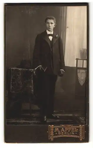 Fotografie M. Appel, Berlin, junger Mann im Anzug stehend mit Handschuhen und Buch in der Hand
