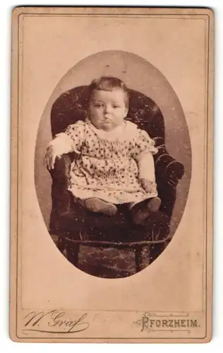 Fotografie W. Graf, Pforzheim, Portrait niedliches Kleinkind im hübschen Kleid auf Sessel sitzend