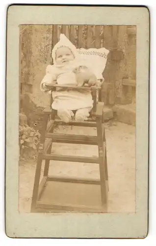 Fotografie unbekannter Fotograf und Ort, Portrait Säugling in Kindersitz mit Spielzeugkaninchen