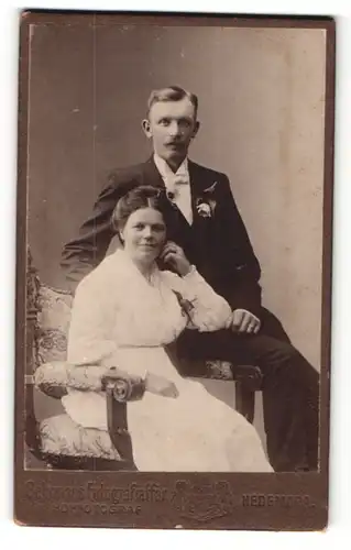 Fotografie Gehrman, Hedemora, Frau im Kleid auf Stuhl sitzend und Mann im Anzug deneben auf Lehne sitzend