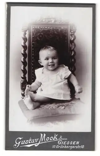 Fotografie Gustav Mook, Giessen, Lächelndes Kleinkind sitzend in einem Stuhl