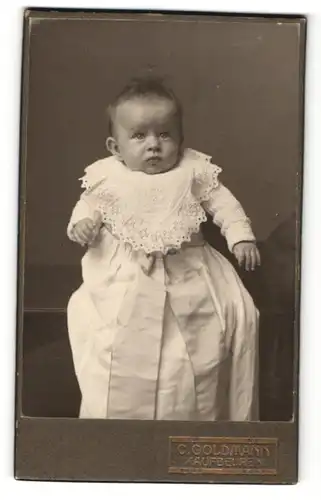 Fotografie C. Goldmann, Kaufbeuren, Baby mit verwundertem Blick im weissen Kleid