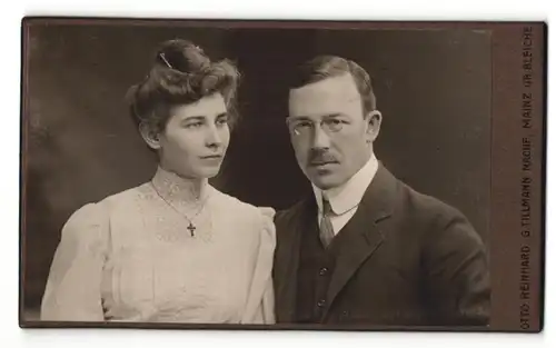 Fotografie Otto Reinhard, Mainz, Frau im Kleid mit Halskette mit Kreuz und Mann im Anzug mit Brille