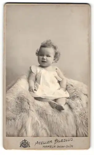 Fotografie Atelier Blesius, Hameln i. W., Portrait lachendes kleines Mädchen mit lockigem Haar auf Fell sitzend