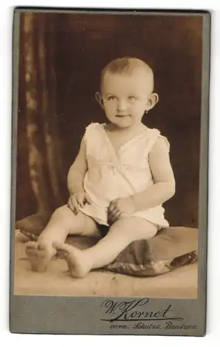 Fotografie W. Kornet, Bautzen, Portrait kleines Mädchen im weissen Hemd auf Kissen sitzend