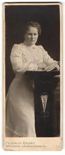 Fotografie Friedrich Ehlers, Solingen, Portrait ernste junge Frau im edlen Kleid am Tisch