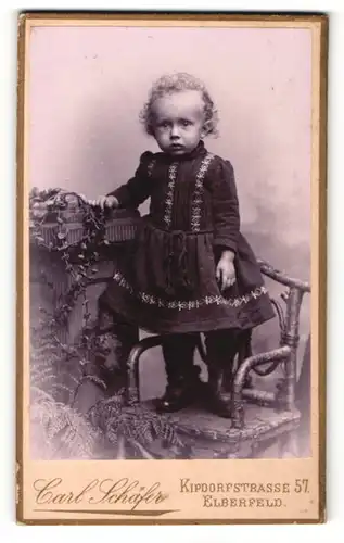 Fotografie Carl Schäfer, Elberfeld, Portrait kleines Mädchen im hübschen Kleid auf Stuhl stehend