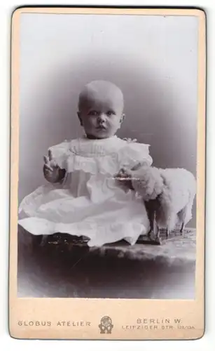 Fotografie Atelier Globus, Berlin, Portrait bezauberndes Kleinkind im weissen Kleidchen mit Spielzeugschaf