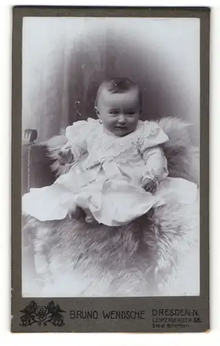 Fotografie Bruno Wendsche, Dresden-N., Portrait süsses Kleinkind mit Ohrringe im weissen Kleidchen auf einem Fell