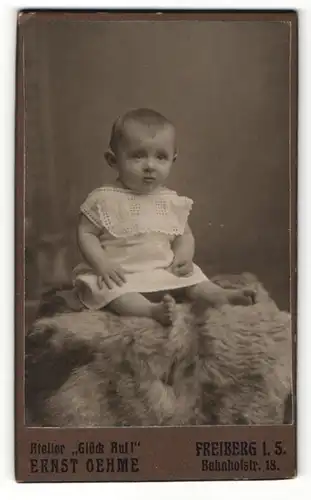 Fotografie Ernst Oehme, Freiberg i. S., Portrait niedliches Kleinkind im weissen Hemd auf Fell sitzend