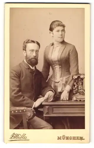 Fotografie F. Müller, München, Portrait elegant gekleidetes Paar am Tisch stehend
