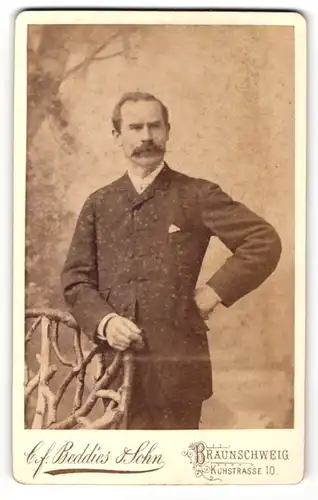 Fotografie C.F. Beddies & Sohn, Braunschweig, Portrait Herr im feinen Anzug an einem Stuhl