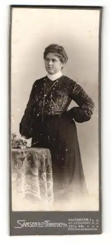 Fotografie Samson & Co., Frankfurt a / M., Portrait hübsch gekleidete Dame mit Blumen an Tisch gelehnt