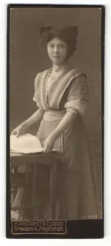 Fotografie Klinkhardt & Eyssen, Dresden-A, Portrait hübsche gekleidete Dame mit Buch an Tisch gelehnt
