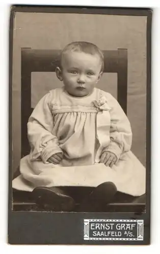 Fotografie Ernst Graf, Saalfeld a/S., Baby im Kleidchen auf Stuhl sitzend