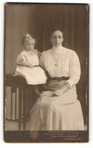Fotografie R. Rosenkranz, Mügeln, Frau im Kleid sitzend mit Kind auf Tisch sitzend neben sich
