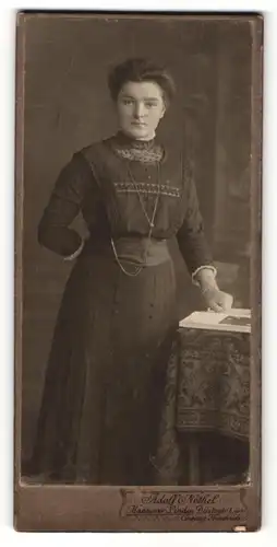 Fotografie Adolf Nothel, Hannover-Linden, Portrait hübsch gekleidete Dame mit Buch an Tisch gelehnt