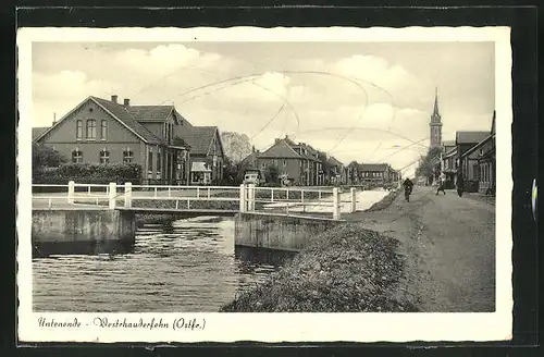 AK Westrhauderfehn / Ostfr., Untenende, Blick auf Ufer mit Brücke, Kirchturm und Häuser