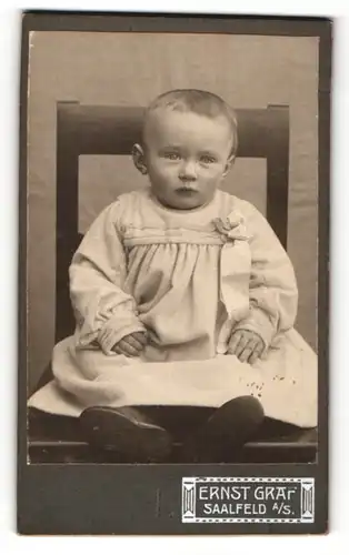 Fotografie Ernst Graf, Saalfeld a. S., Portrait niedliches Kleinkind im Kleid mit Schleife