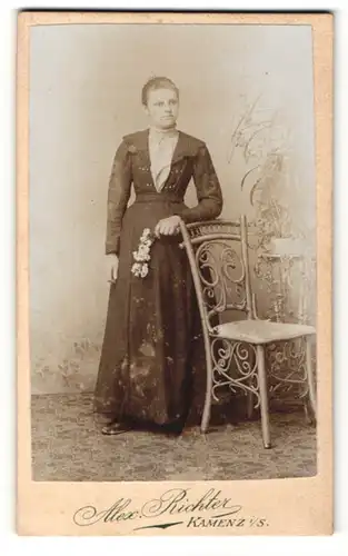 Fotografie Alex. Richter, Kamenz i / S., Portrait elegant gekleidete Dame mit Blume an Stuhl gelehnt