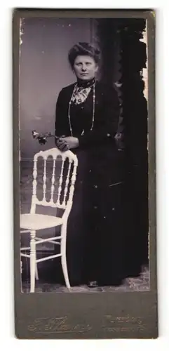 Fotografie F. Flarupo, Flensburg, Portrait Dame im schwarzen Kleid an einem Stuhl